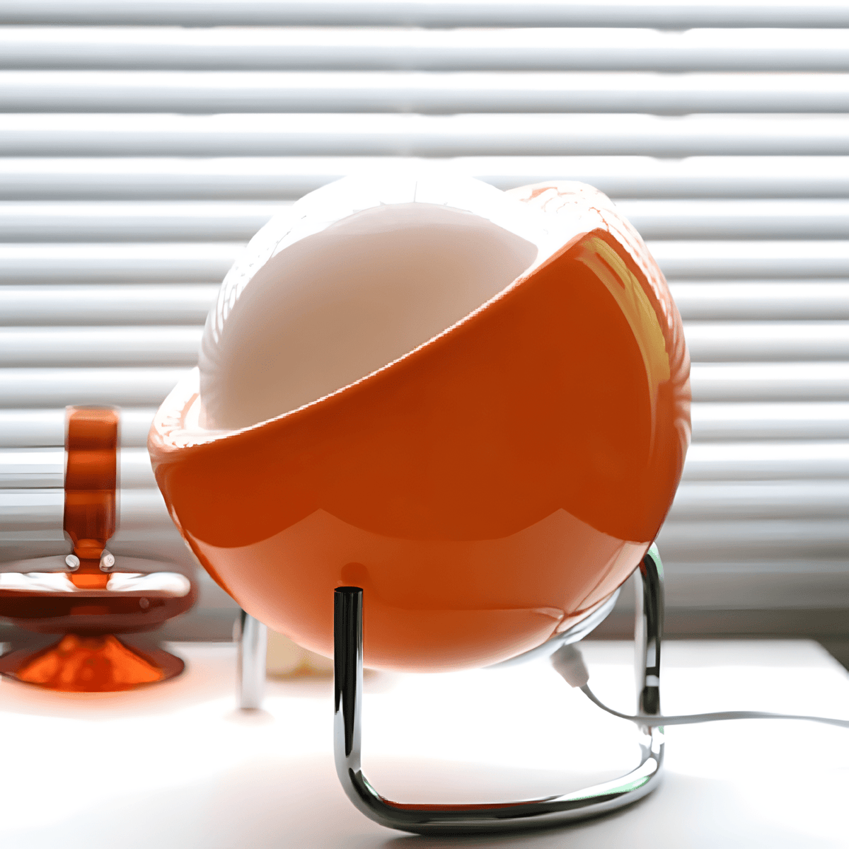 Bauhaus lampada da tavolo in vetro arancione e metallo cromato: lampada davanti a una finestra con veneziana, vista laterale - Luximode