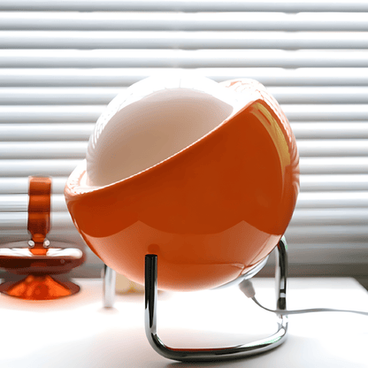 Bauhaus lampada da tavolo in vetro arancione e metallo cromato: lampada davanti a una finestra con veneziana, vista laterale - Luximode