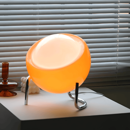 Bauhaus lampada da tavolo in vetro arancione e metallo cromato: lampada accesa su una base bianca davanti a una veneziana - Luximode