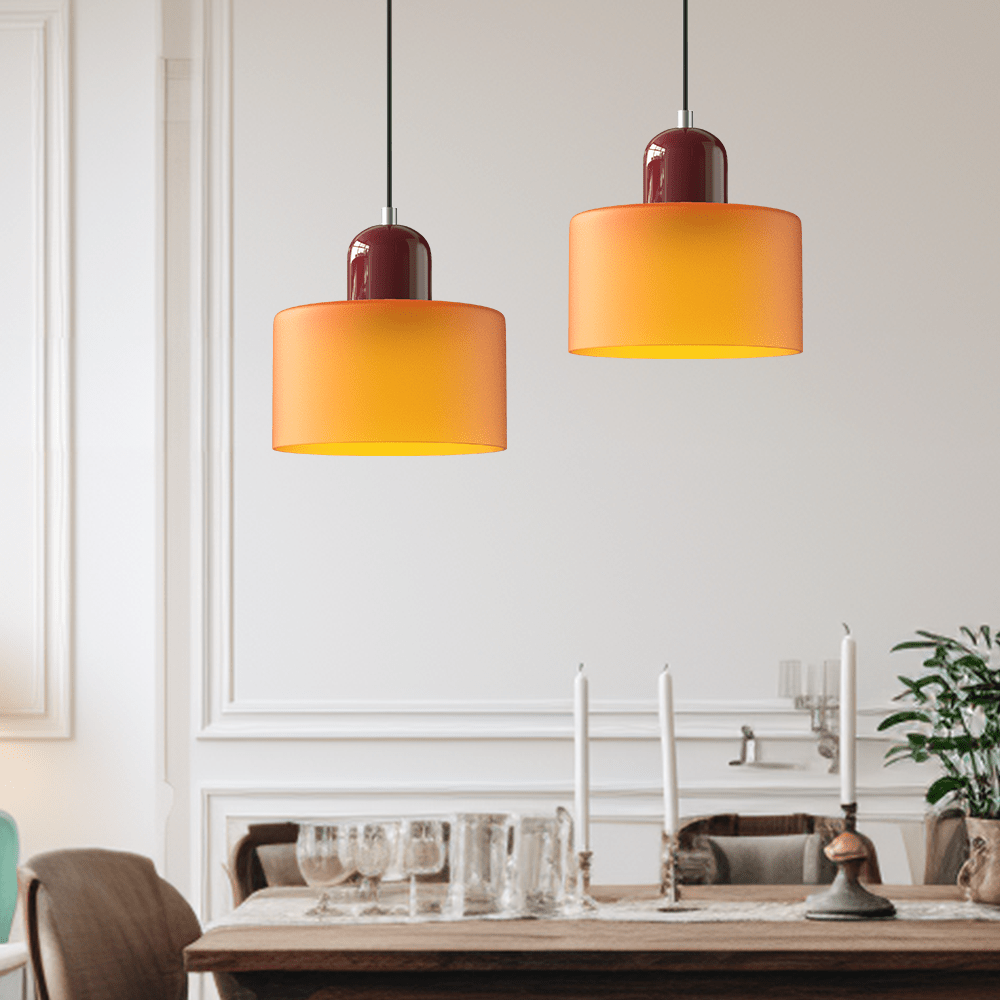 Due lampade Croma in vetro arancione sospese sopra un tavolo da pranzo apparecchiato