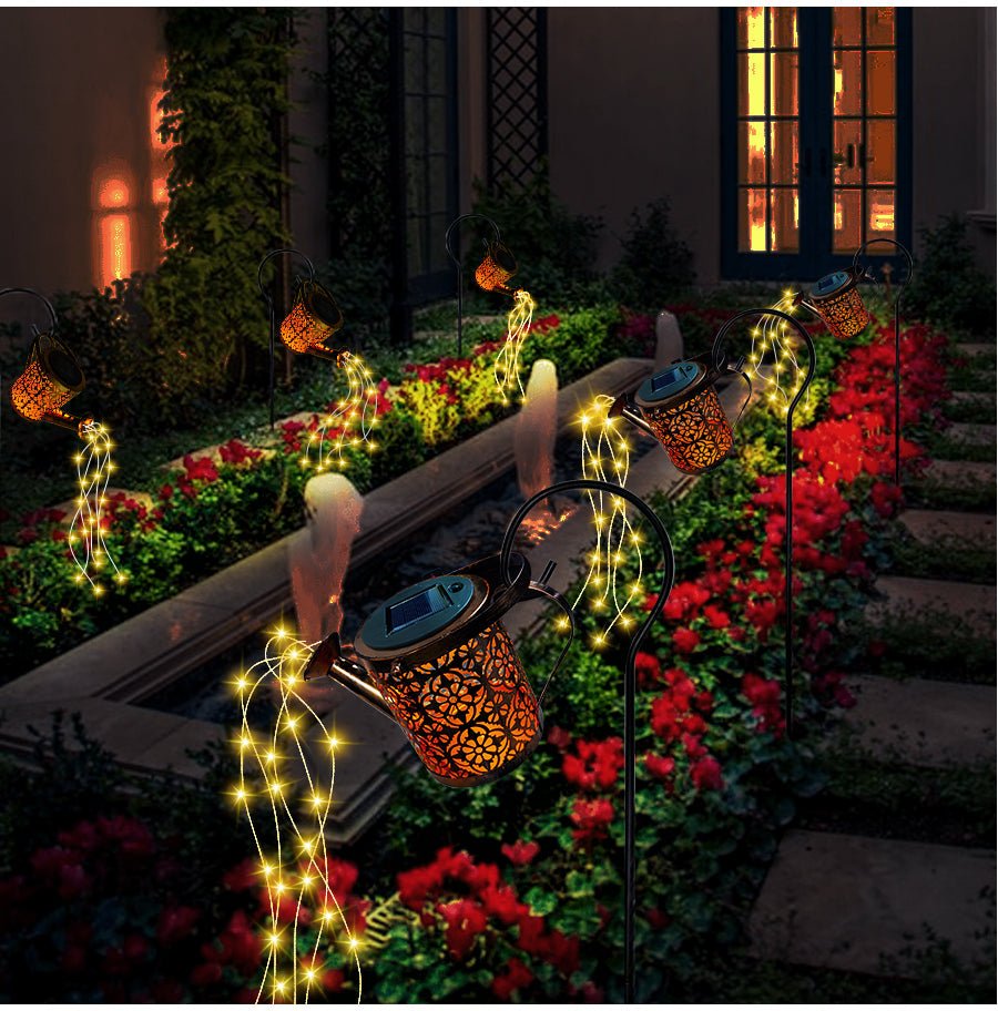 EnchantedCan lampada solare da esterno a forma di annaffiatoio con cascata di micro LED: annaffiatoio acceso tra fiori rossi davanti a una casa - Luximode