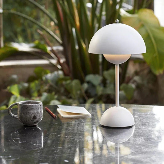 FungiLamp lampada da tavolo ricaricabile a forma di fungo in ferro e plastica: versione bianca accesa su un tavolo di marmo accanto a una pianta - Luximode