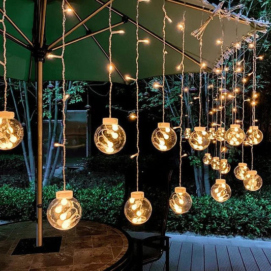 LumiFae catena luminosa LED impermeabile da esterno con sfere pendenti: catena accesa sotto un ombrellone in un giardino con luce calda - Luximode