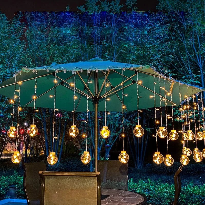 LumiFae catena luminosa LED impermeabile da esterno con sfere pendenti: catena accesa appesa a un ombrellone in una terrazza di sera - Luximode