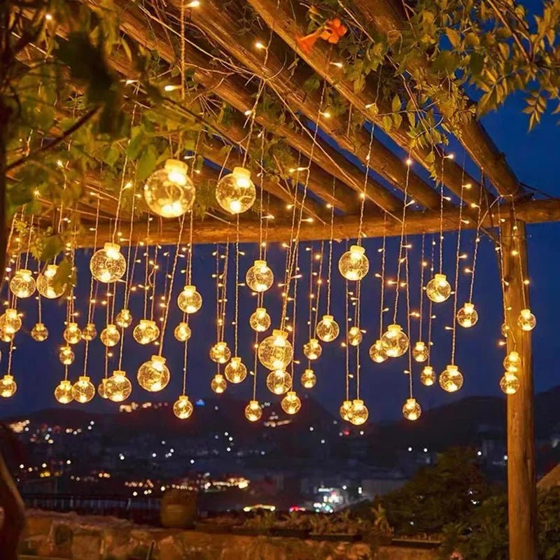 LumiFae catena luminosa LED impermeabile da esterno con sfere pendenti: catena accesa tra le piante di un pergolato con vista sulla citta di notte - Luximode