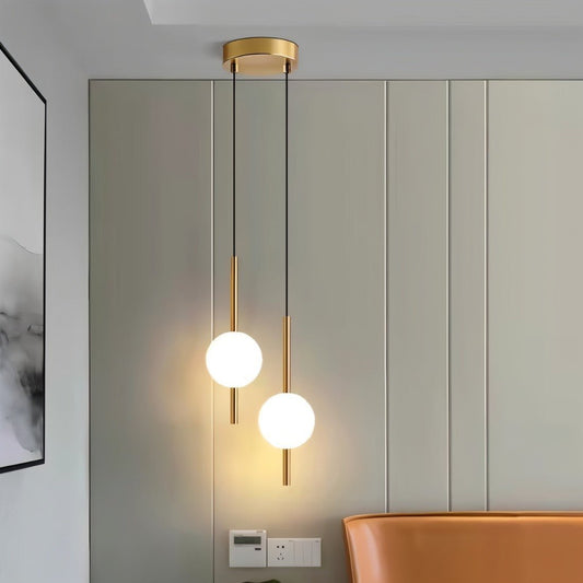 Lampada a sospensione LuminousTwins in ottone dorato a due sfere, accesa sopra una poltrona in cuoio