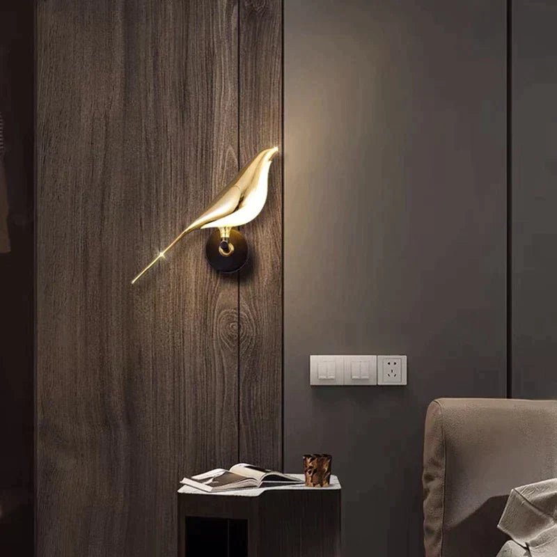 Applique MrBird accesa su parete in legno accanto alla poltrona