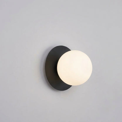 Applique Ostuni nera su parete neutra: disco in metallo e sfera in vetro satinato