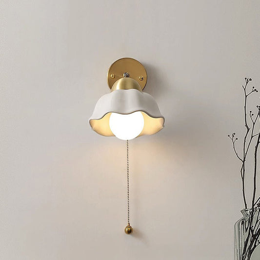 RetroFrench applique da parete in stile francese in ferro e acrilico, oro e bianco: applique accesa con paralume bianco ondulato e catenella, accanto a rami secchi - Luximode
