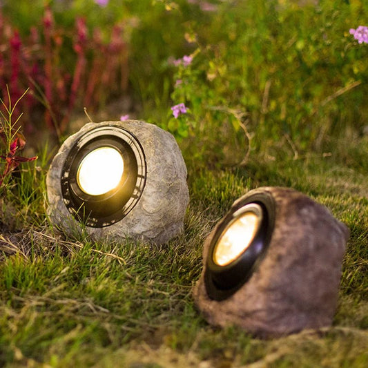 RockyLight lampada solare da esterno a forma di pietra: due lampade accese tra i fiori di un'aiuola al tramonto - Luximode