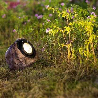 RockyLight lampada solare da esterno a forma di pietra: lampada accesa tra le piante fiorite di un giardino al tramonto - Luximode