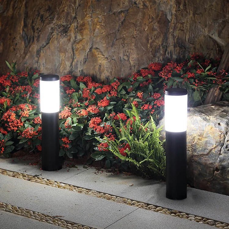SolarGlow lampada solare da giardino impermeabile in acciaio: due lampade accese lungo un'aiuola fiorita davanti a un muro di pietra - Luximode