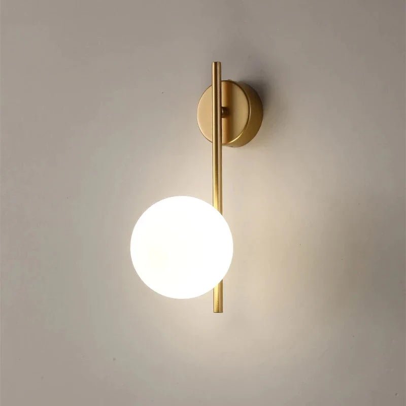 Applique SOLVIA oro con sfera opalina accesa su parete chiara
