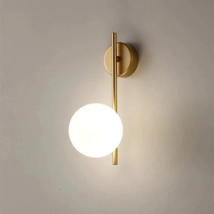 Applique SOLVIA oro con sfera opalina accesa su parete chiara
